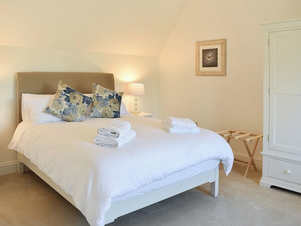 A neatly made bed with floral pillows, a bedside lamp, and folded towels.