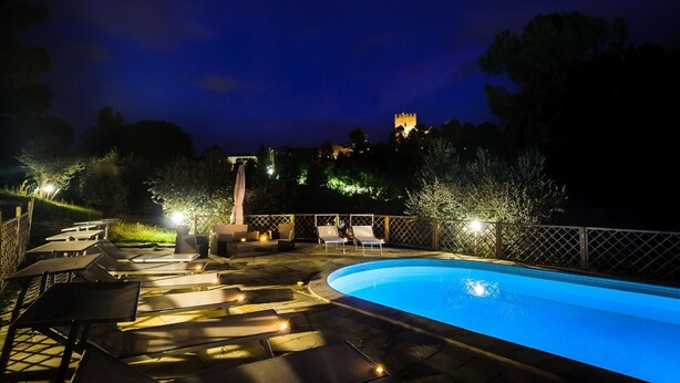 A nighttime swimming pool area with lounge chairs and a view of a castle in the background. - Villa Mery, Holiday house in the hills of the Rimini Riviera, with private pool (Mondaino)