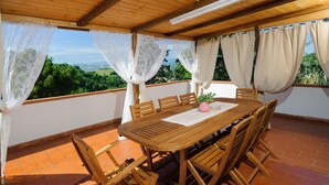 A wooden table with chairs, a pink vase, and a white tablecloth on a terrace with a view of greenery. - Villa Mery, Holiday house in the hills of the Rimini Riviera, with private pool (Mondaino)