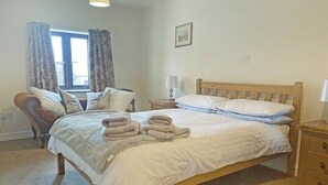 Une chambre à coucher avec un lit, une chaise, une table de chevet, une lampe et une fenêtre avec des rideaux.