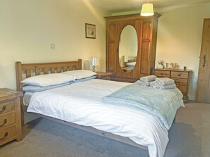 Un lit bien fait, avec du linge de lit blanc, une tête de lit en bois, une table de chevet avec une lampe, un miroir et une commode avec des serviettes.