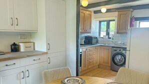 Une cuisine avec des meubles blancs, un plan de travail en bois, un lave-linge et une table à manger dressée avec des assiettes et des verres.