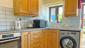Une cuisine compacte avec des meubles en bois, un four à micro-ondes encastré, un grille-pain et un lave-linge à chargement frontal.