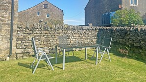 Un bâtiment en pierre doté d’une horloge, un mur en pierre et un espace verdoyant avec une table et des chaises.