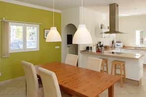A modern kitchen with a wooden dining table and chairs, a central island, and pendant lighting.