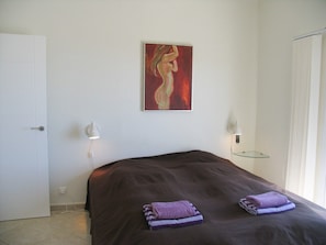 A bedroom with a bed, a painting on the wall, and a bedside table with a lamp. - Casa Turbolina  | Beautiful Country House with Pool, BBQ & Stunning Valley & Sea Views (Algarrobo)