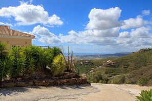 A house with a stone wall and tropical plants, overlooking a hilly landscape with a clear sky. - Casa Turbolina  | Beautiful Country House with Pool, BBQ & Stunning Valley & Sea Views (Algarrobo)