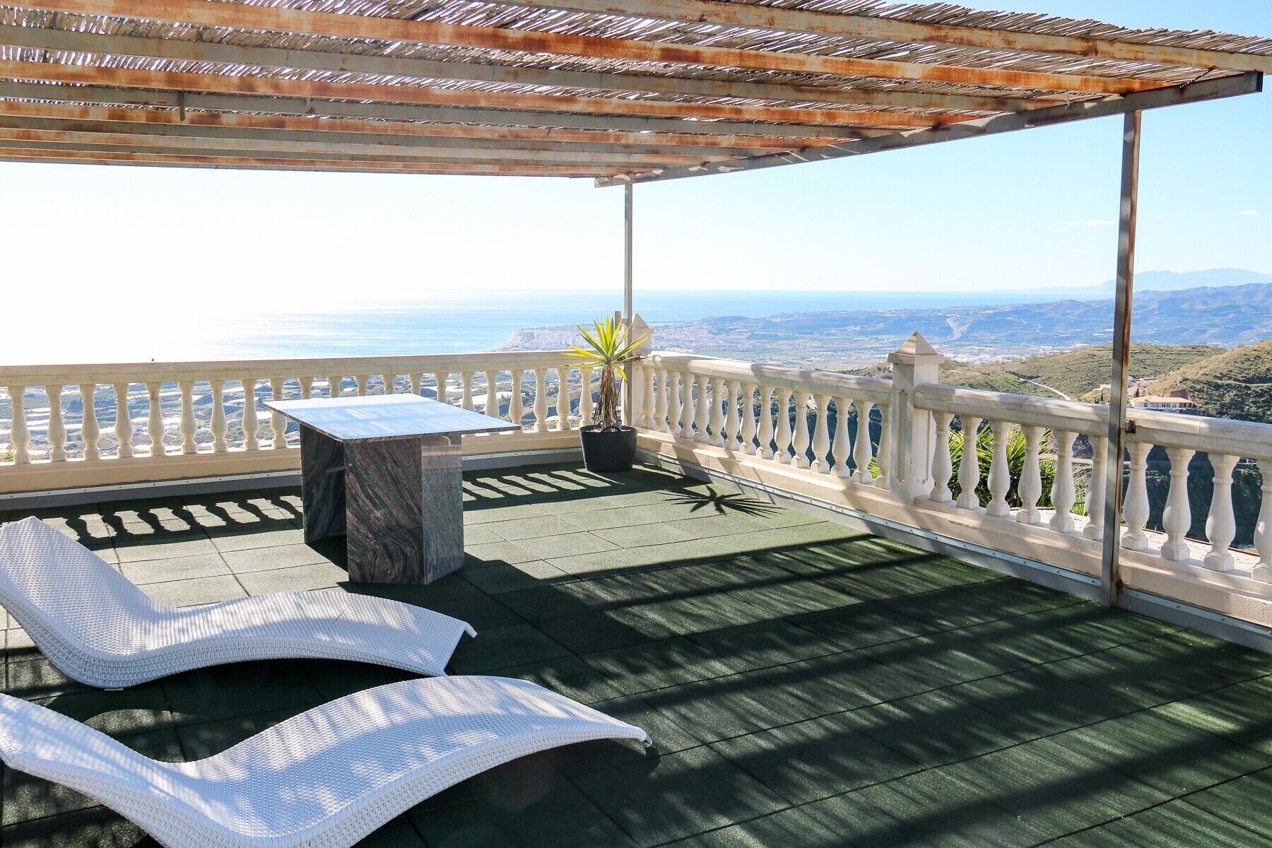 A covered outdoor area with a table and two lounge chairs, overlooking a scenic view.