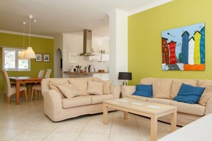 A living room with a beige sofa, a wooden coffee table, and a painting of colorful buildings on the wall.