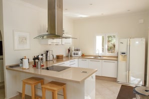 A modern kitchen with a central island, white cabinetry, stainless steel appliances, and a window providing natural light. - Casa Turbolina  | Beautiful Country House with Pool, BBQ & Stunning Valley & Sea Views (Algarrobo)