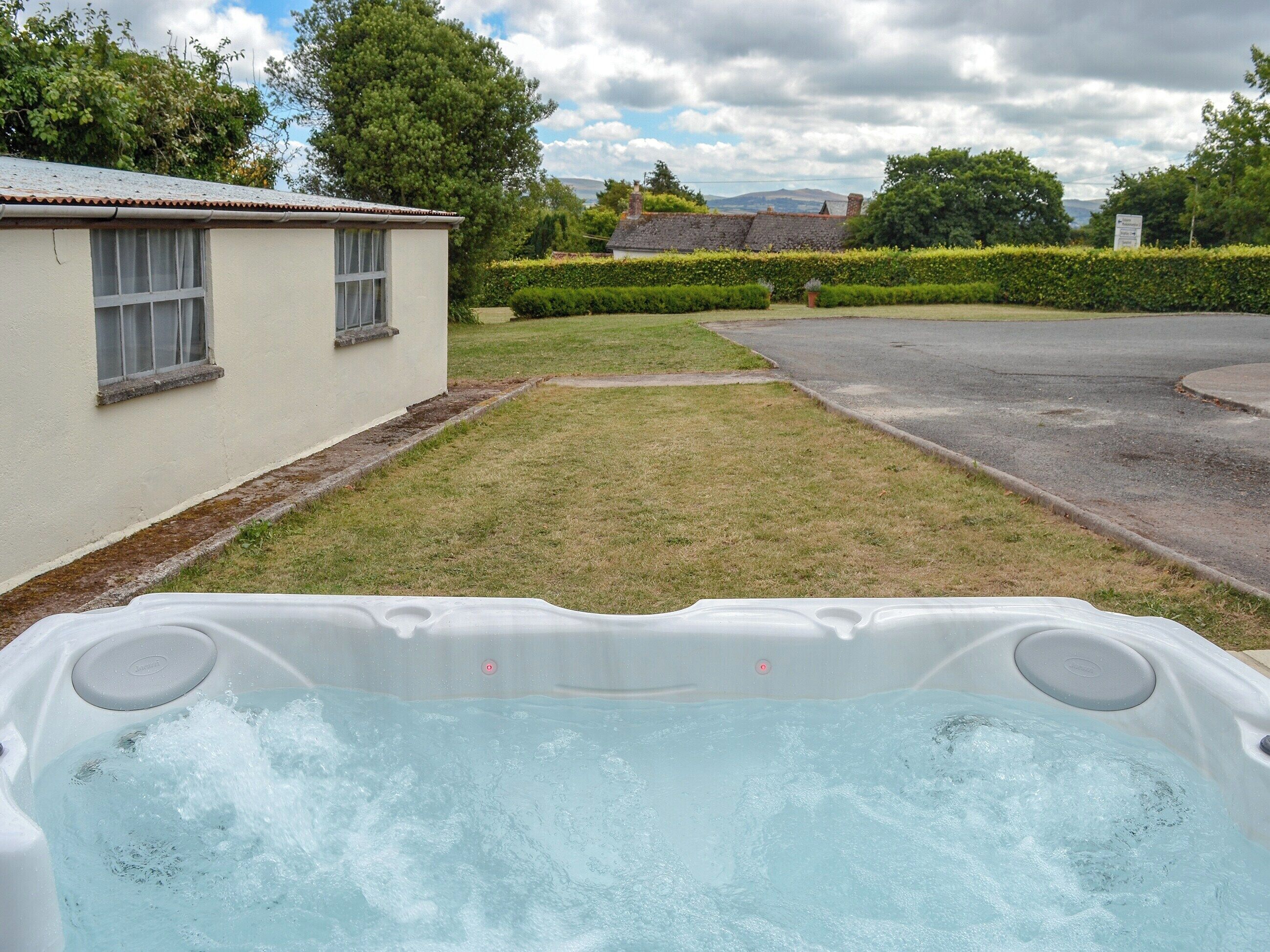 Un jacuzzi dans un jardin, avec une maison et une haie en arrière-plan.
