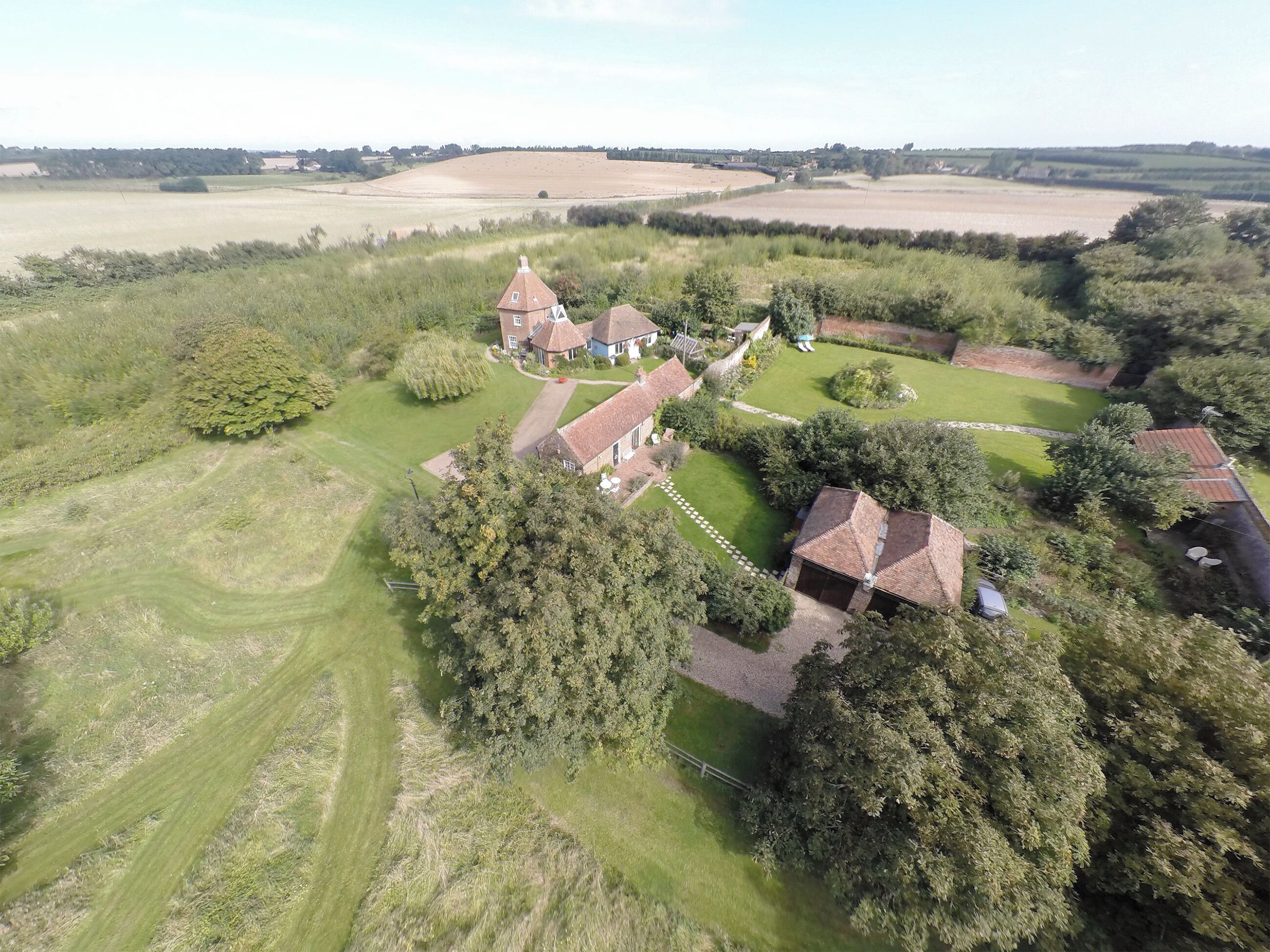 Luchtbeeld van een landgoed met meerdere gebouwen, groene gazons en omliggende velden.