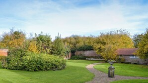 A well-maintained garden with a winding gravel path, a stone fountain, and a brick building with a red-tiled roof. - Gamekeeper's Cottage (Staple, near Wingham)