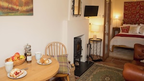 A cozy room with a dining table set for breakfast, a bed with a red floral bedspread, and a fireplace. - Gamekeeper's Cottage (Staple, near Wingham)