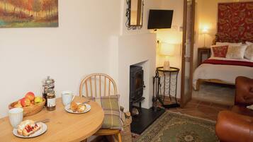 A cozy room with a dining table set for breakfast, a bed with a red floral bedspread, and a fireplace.
