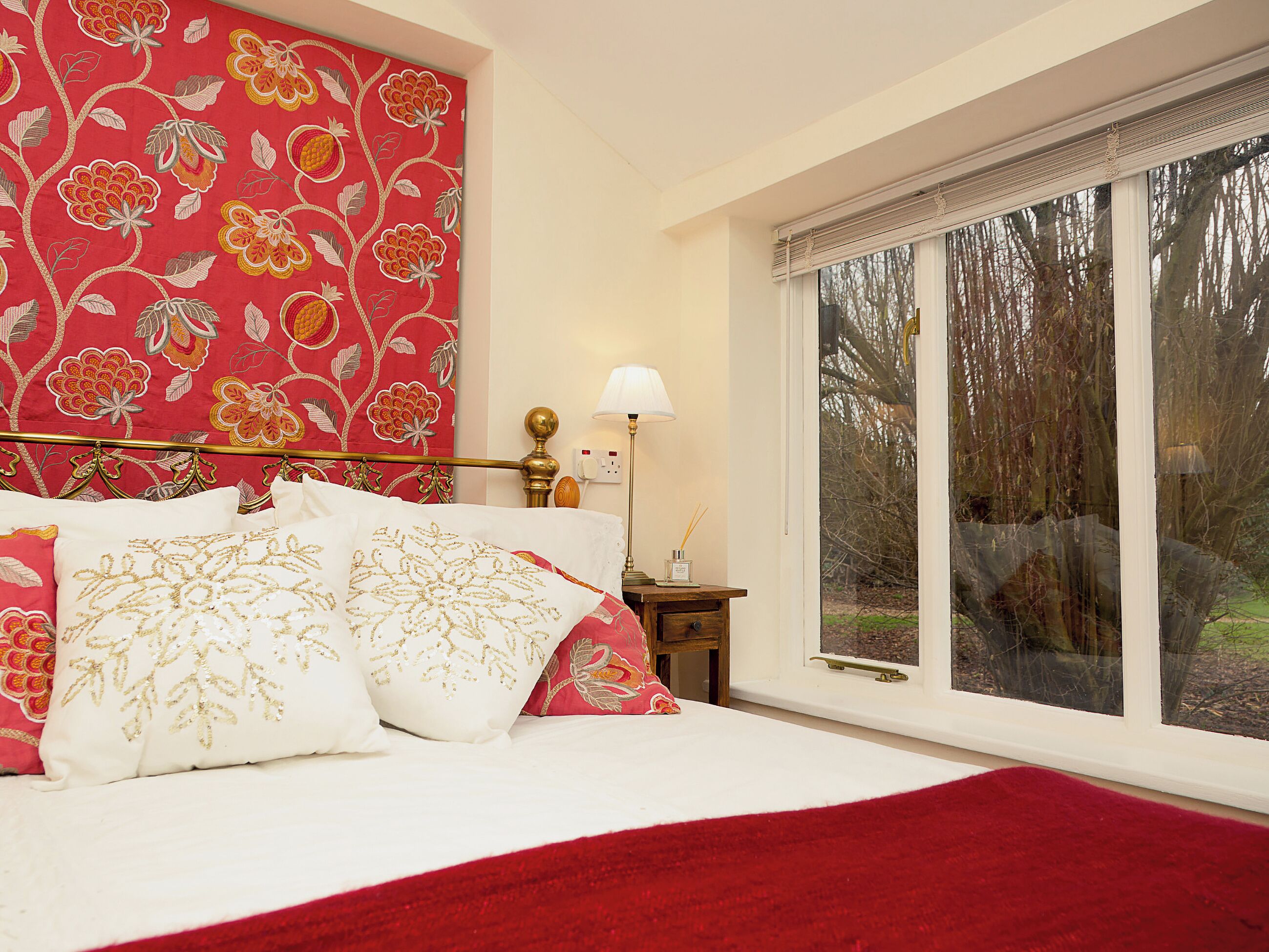 Une chambre avec une grande fenêtre, un lit avec une literie rouge et blanche, et un mur orné d’un motif floral.