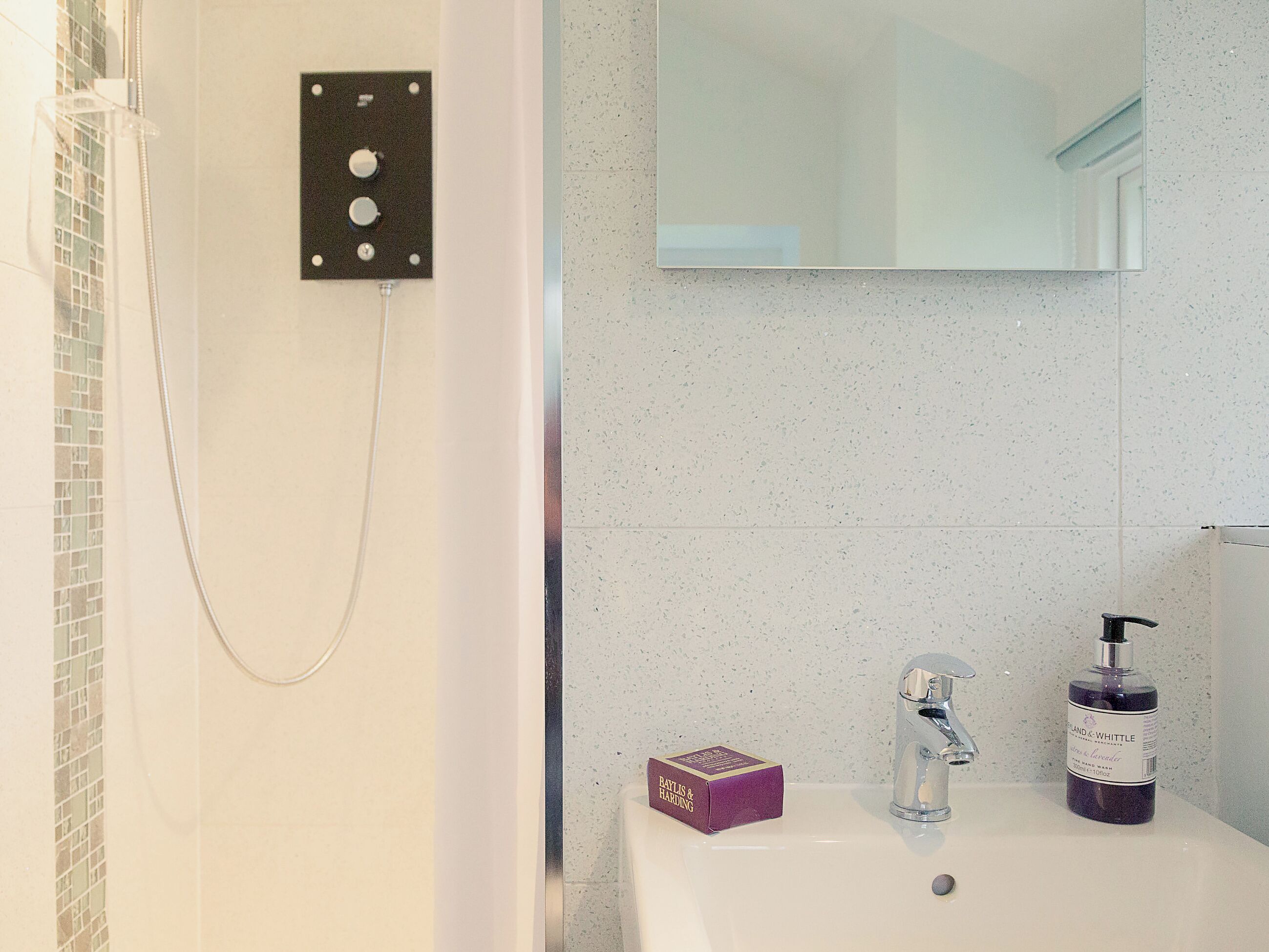 Une salle de bain équipée d’une douche, d’un lavabo, d’un miroir et d’articles de toilette.