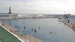 A large public swimming pool with a monument in the background, surrounded by a white fence and a promenade. - 3 bedroom accommodation in Penzance (Penzance)