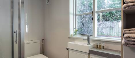 A modern bathroom with a glass shower enclosure, a toilet, a sink with a window above, and a towel rack.