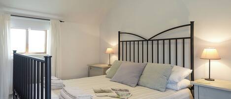 Un dormitorio con una cama, dos mesitas de noche, una mesilla auxiliar, una ventana con cortinas y un radiador.