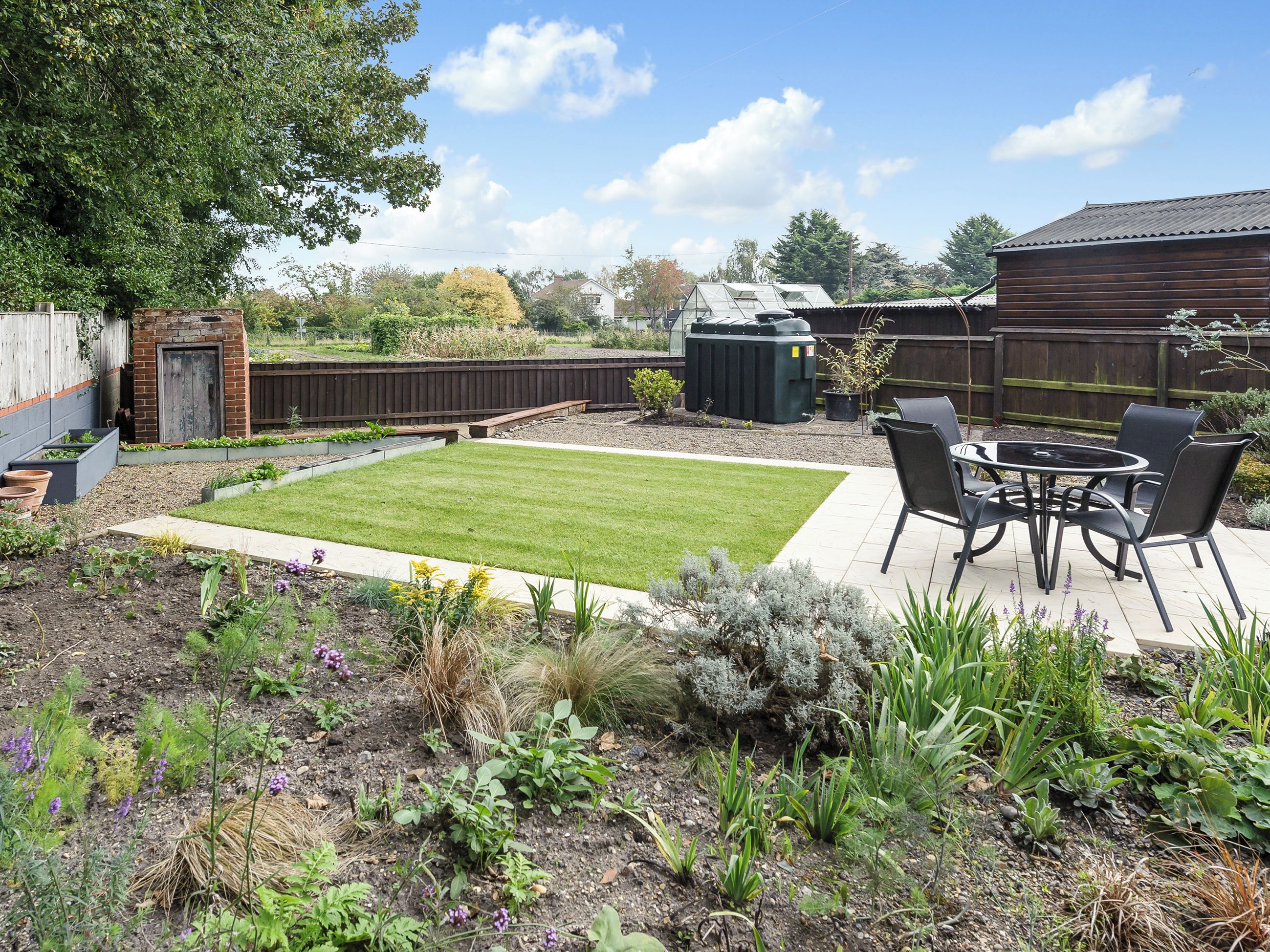 Un jardin avec une terrasse, une pelouse et diverses plantes.