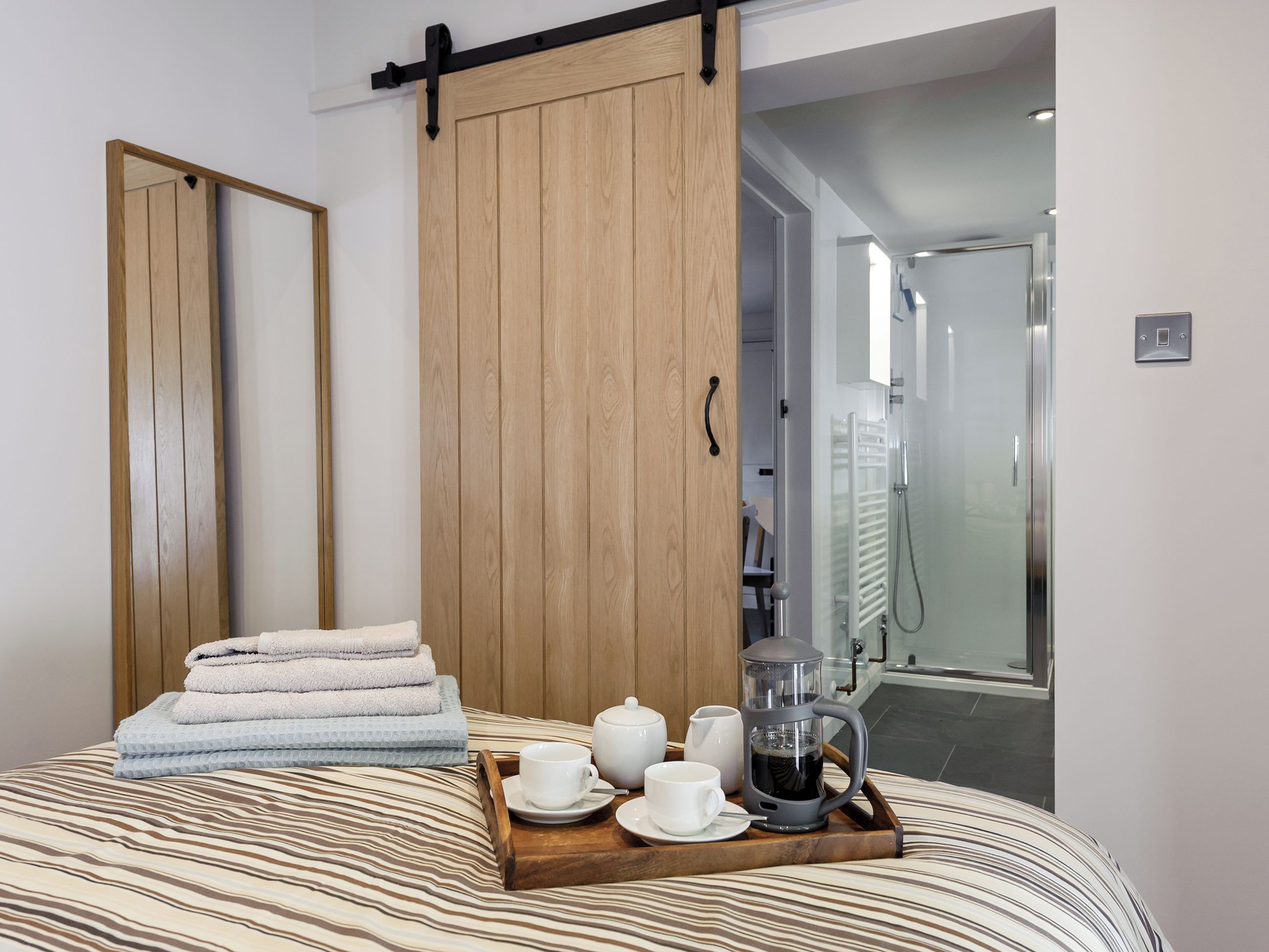 A hotel room with a bed, a wooden sliding door, a tray with tea set, and a shower area.