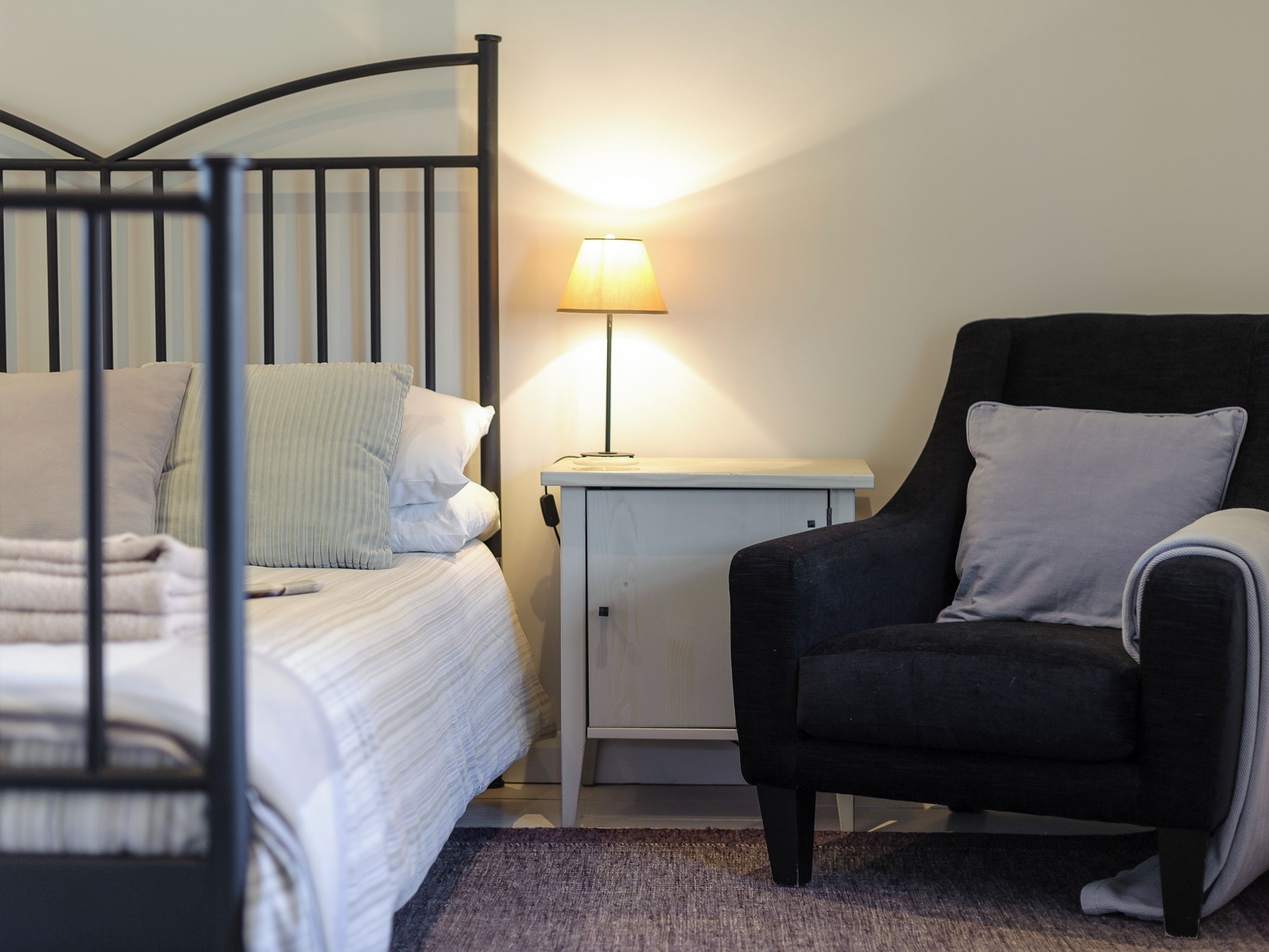 A bedroom with a bed, a nightstand, a lamp, and a chair.