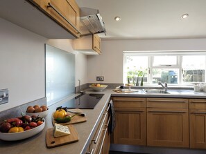 A modern kitchen with wooden cabinets, a built-in oven, a large window, and various kitchen items on the counter. - 2 bedroom accommodation in Blythburgh, near Southwold (Blythburgh, near Southwold)