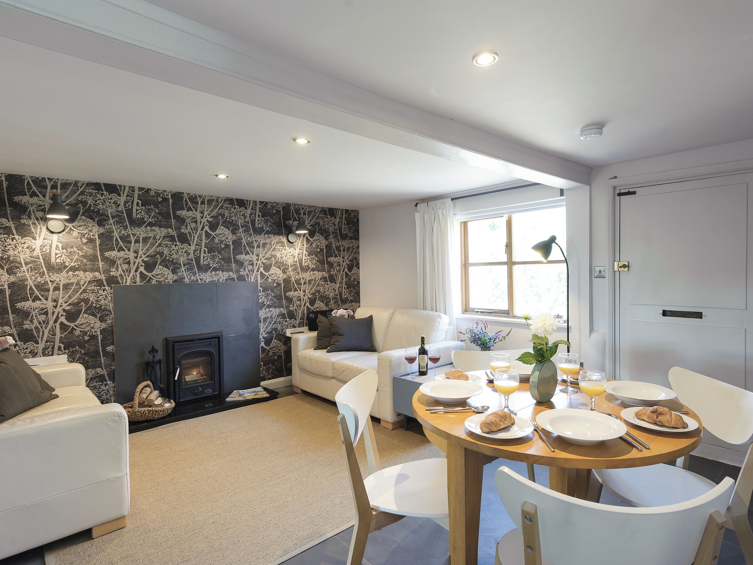A modern living room with a fireplace, a dining area with breakfast set, and a large window.