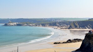 Un paysage côtier avec une plage de sable, des falaises et une vue lointaine sur des bâtiments et des éoliennes.