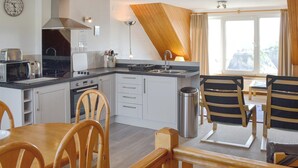 Une cuisine compacte dotée d’appareils électroménagers modernes, un coin repas avec des chaises en bois et une vue sur une falaise par la fenêtre.