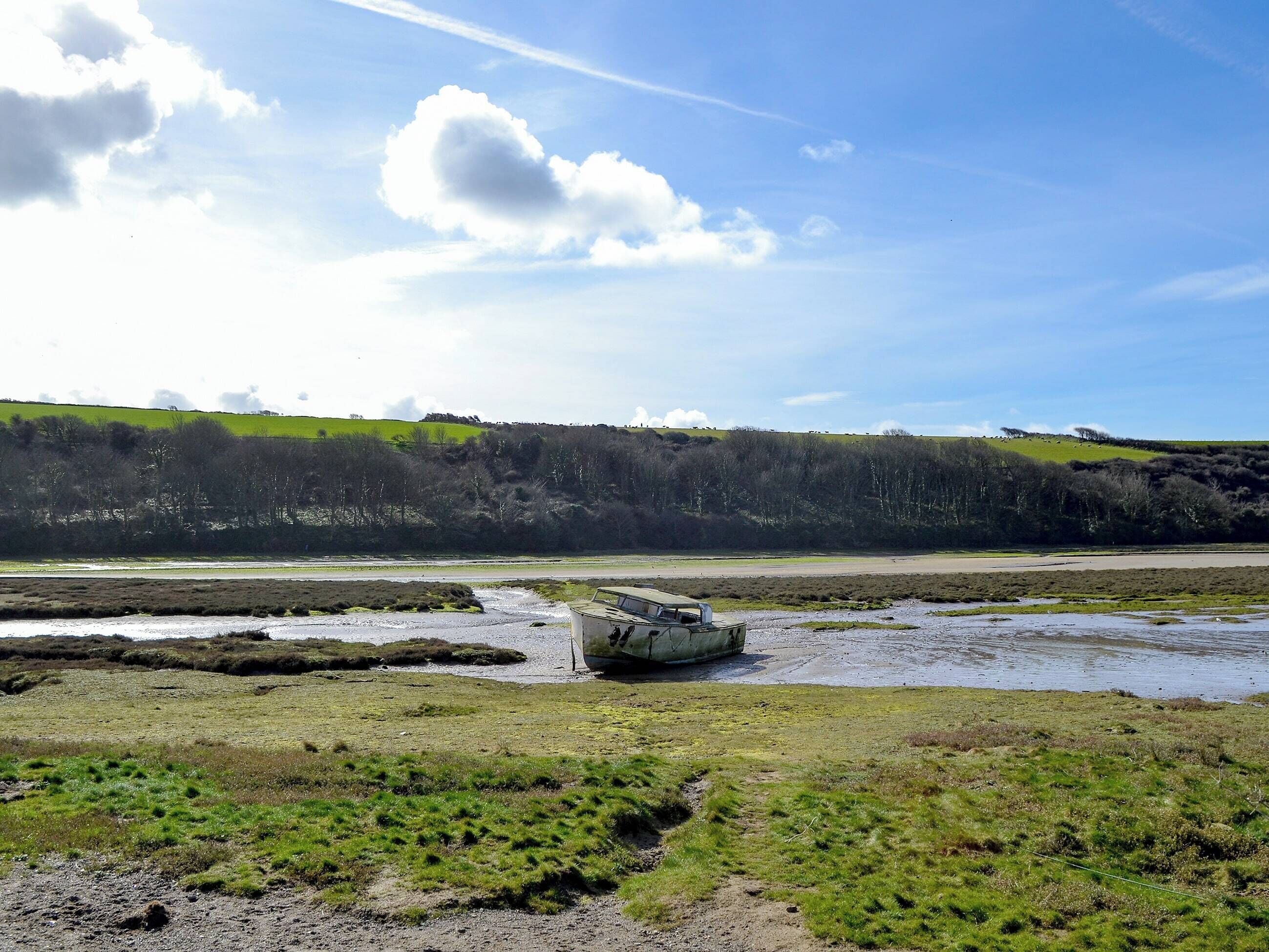 A boat stranded on a muddy shore with a green landscape and hills in the background.