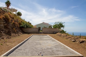 A bocce court with a concrete boundary and scattered bocce balls, surrounded by a hillside with sparse vegetation and a building in the background. - Casa Bonita | Authentic Andalusian House (Algarrobo)