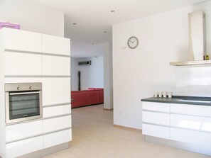 A modern kitchen with built-in appliances, a red sofa in the background, and a wall clock. - Casa Bonita | Authentic Andalusian House (Algarrobo)