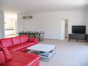 A living room with a red sofa, a white coffee table with magazines, a dining table with chairs, a TV on a cabinet, and a door leading to another room. - Casa Bonita | Authentic Andalusian House (Algarrobo)