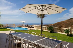 A poolside area with a table and chairs, a large umbrella, and a view of the ocean. - Casa Bonita - 4 bedroom Country House in Authentic Andalucia, Malaga (Algarrobo)