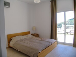 A bedroom with a wooden bed, a bedside table with a lamp, and a view of a building through a window. - Casa Bonita - 4 bedroom Country House in Authentic Andalucia, Malaga (Algarrobo)