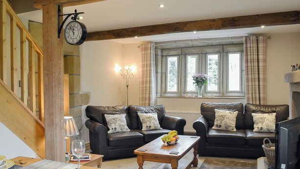 A cozy living room with two leather sofas, a wooden coffee table, and a dining area with a table set for two. - Little Grans Cottage (Ickornshaw, near Cowling)