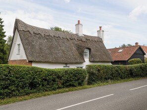 A traditional thatched-roof cottage with a white exterior, a small window, and a chimney.
