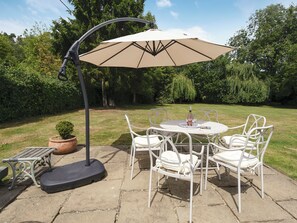 An outdoor patio with a round table and white chairs, a large umbrella, and a potted plant.