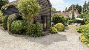 A house with a gravel driveway, a wooden door, and a garden with various plants and a patio table. - 3 bedroom accommodation in Sternfield, near Aldeburgh (Sternfield, near Aldeburgh)