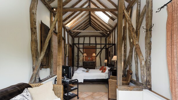 A rustic room with exposed wooden beams, a bed with white linens, a wicker chair, and a radiator. - 3 bedroom accommodation in Sternfield, near Aldeburgh (Sternfield, near Aldeburgh)