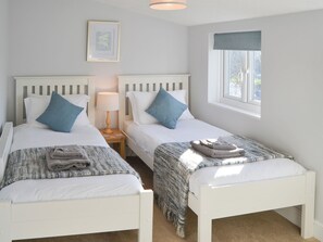 A room with two single beds, a bedside table with a lamp, a framed picture on the wall, and a window with a view.