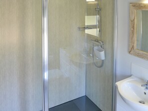 A modern bathroom with a glass shower enclosure, a white sink, and a mirror with a wooden frame.