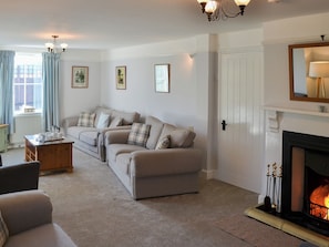 A living room with a beige sofa set, a coffee table, a fireplace, and a chandelier.
