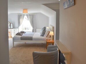 A bedroom with a bed, bedside table, chair, and a window with curtains.