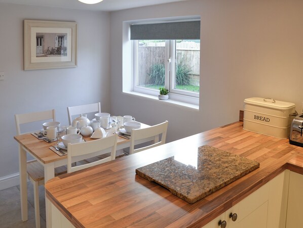A kitchen with a wooden table set for breakfast, a window with a view of the backyard, and a bread box labeled 'BREAD'.