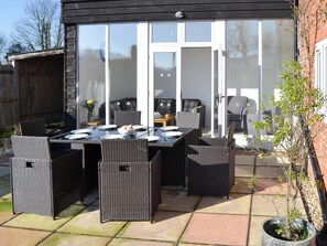 An outdoor patio with a dining table and chairs, a grill, and a potted plant.