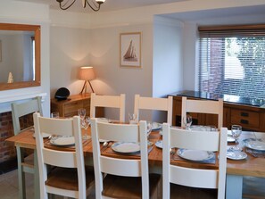 A dining area with a wooden table set for four, white chairs, and a lamp on a tripod stand.
