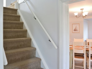 A staircase with carpeted steps and a handrail, leading to a dining area with a table set for two and a chandelier.